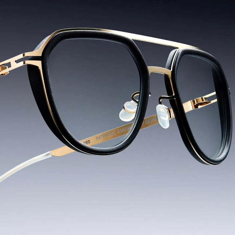 Gros plan sur la charnière sans vis d'une monture Mykita noire et dorée — disponible chez Bar à Lunettes Québec