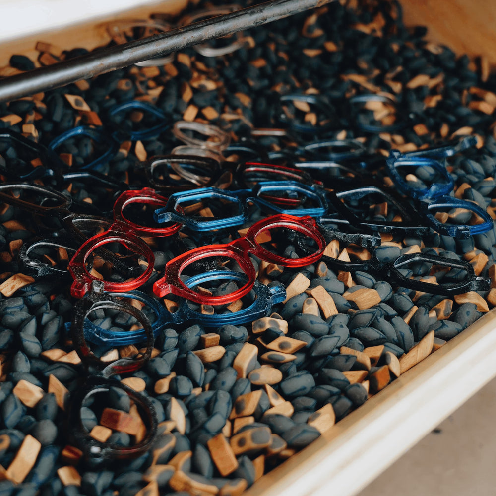 Montures de lunettes en acétate rouge et bleu parmi des granulés d'acétate de cellulose bruts